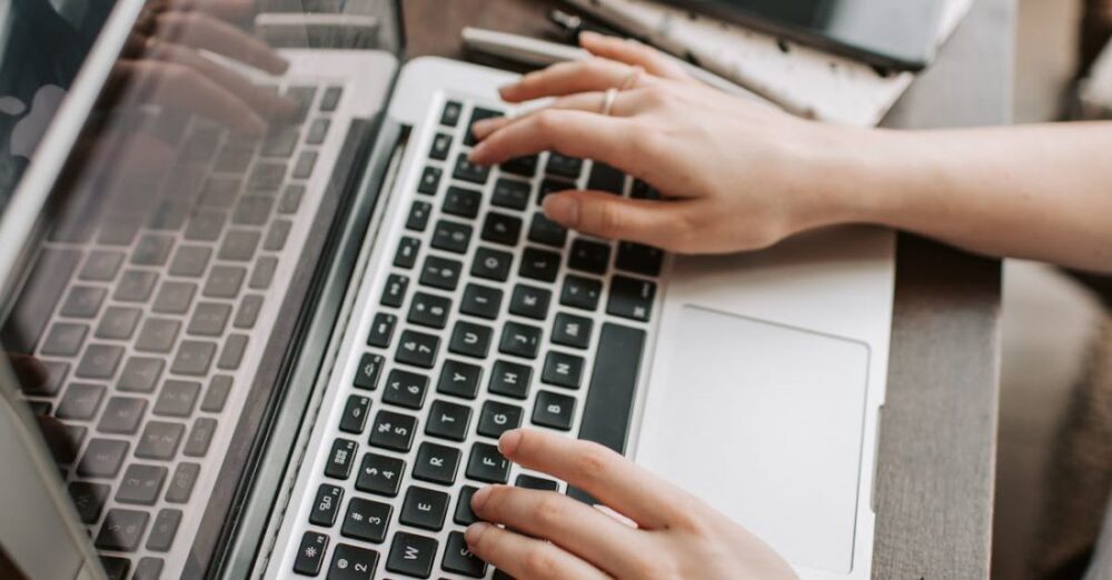 Remote Workers - From above of unrecognizable woman sitting at table and typing on keyboard of computer during remote work in modern workspace